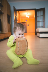 Child biting bread. Little girl with a bun of bread sitting on the wooden floor. He looks into the...
