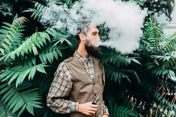 Young man with beard vaping an electronic cigarette outdoor. hipster smoke vaporizer.