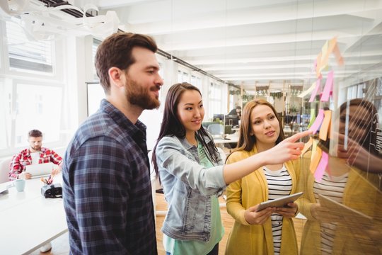 Coworkers looking at sticky notes pointed by female photo editor
