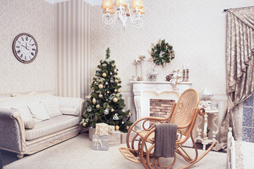 Cozy living room in holiday time. Christmas tree with cones, balls, Garland standing near fireplace, lot of presents under it. On the one wall hangs a needles wreath on the other is watches over sofa