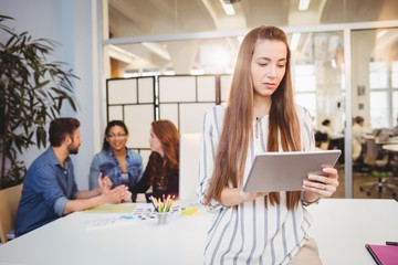 Businesswoman using digital tablet against coworkers 