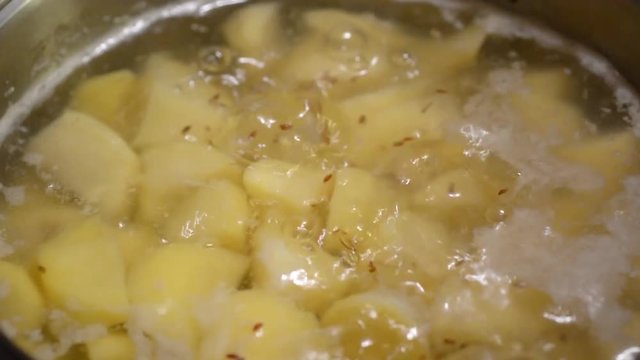 Closeup of boiling sliced potatoes in hot water with caraway seeds.