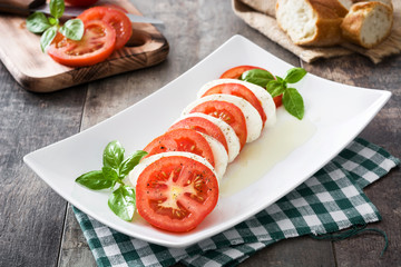 Caprese salad with mozzarella cheese, tomatoes and basil on rustic wooden table

