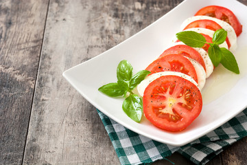 Caprese salad with mozzarella cheese, tomatoes and basil on rustic wooden table

