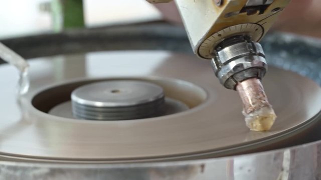 Closeup of diamond held by dop being polished on rotating automatic cast iron lap