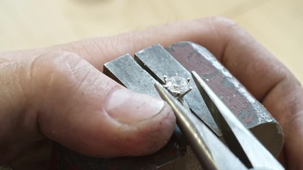 Closeup of hands of jeweler using pliers to bend the prongs gently over the crown of the stone during making silver ring