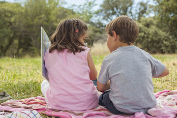 Rear view of two little kids sitting on a towel in the grass.