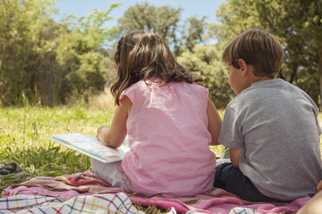 Rear view of two little kids sitting on a towel in the grass.