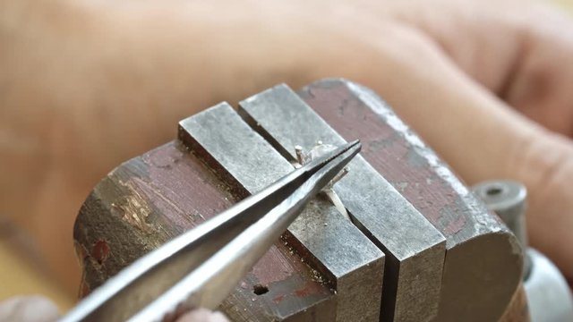 Closeup of hands of jeweler setting a diamond into ring setting with tweezers
