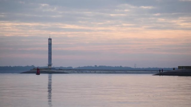 Time lapse of early morning with colorful clouds, people on shore, obviously fishermen, and lighthouse
