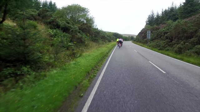 A stabilised view of a group of cycling athletes out on a training ride on country roads in the UK with cars over taking them.