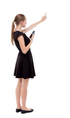 Fototapeta premium back view of pointing young beautiful woman and using a mobile phone. girl watching. Rear view people collection. backside view of person. Isolated over white background. 