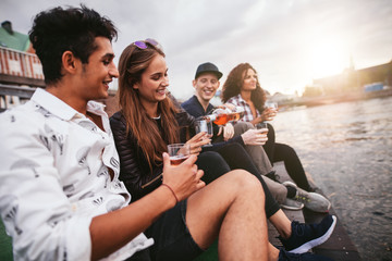 Obraz na płótnie Canvas Friends sitting outdoors on jetty and having drinks