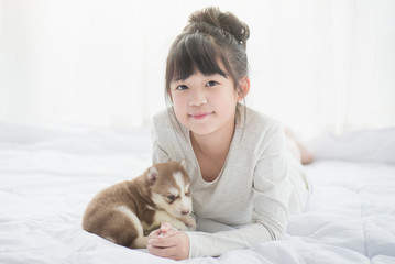 asian girl lying with two siberian husky puppies on bed