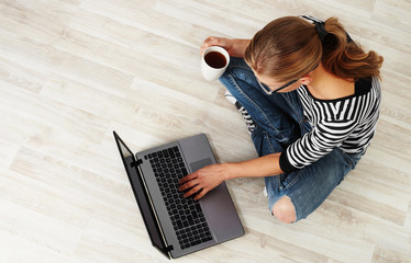 Young woman with coffee mug sitting on the floor with laptop. Concept of distant work, lifestyle...