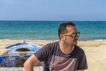 Young man on stylish outfit sitting on an abandoned fishing boat