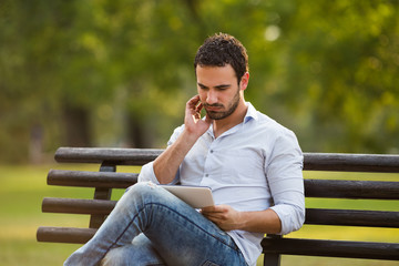 Worried businessman is sitting at the park and using digital tablet.
