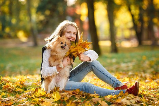 Cute Teenager girl walks with her spitz Dog in Autumn park. Sunny day, selective focus