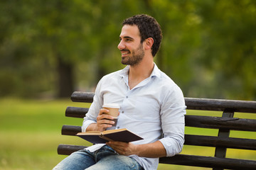 Obraz premium Young businessman enjoys is on a coffee break and he enjoys reading a book and sitting at the park. 