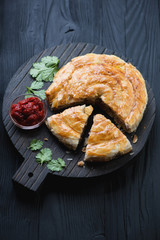 Serving board with sliced burek pie over black wooden background