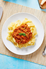 Tagliatelle with Bolognese sauce in white dish on blue wooden table