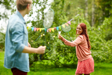 happy friends playing badminton at summer garden