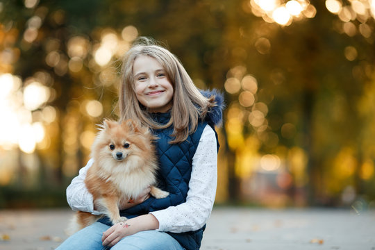 Cute Teenager girl walks with her spitz Dog in Autumn park. Sunny day, selective focus
