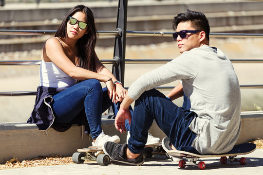 Young Couple Skateboarding In The Street.