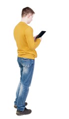 back view of standing young man with tablet computer in the hands of. Rear view people collection.  backside view of person.  Isolated over white background.