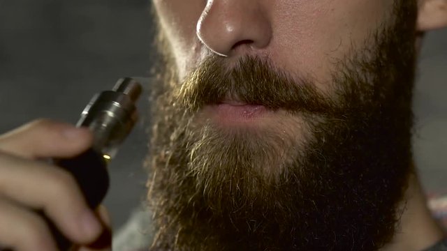 Young man with beard vaping an electronic cigarette. Vaper hipster smoke vaporizer in slow motion