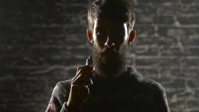 Young man with beard vaping an electronic cigarette. Vaper hipster smoke vaporizer in slow motion