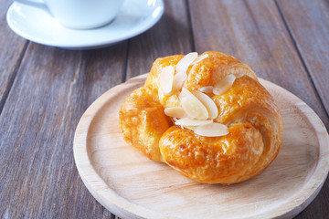 Close up of breakfast with fresh croissant with sliced almonds on a wooden table.