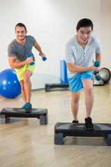 Two men doing step aerobic exercise with dumbbell on stepper