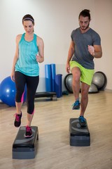 Man and woman doing step aerobic exercise on stepper 