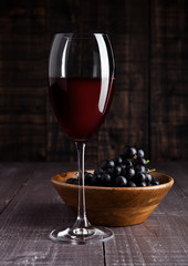 Glass of red wine with grapes in bowl on wood