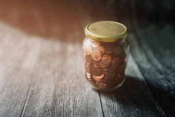 Coins in a closed vintage bottle with filter effect retro against wooden background