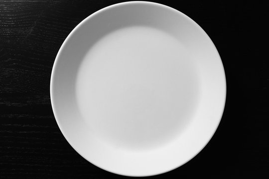 Empty white plate on black wooden table