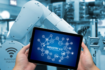 Industry 4.0 concept .Man hand holding tablet with Infographic Industry4.0 icons screen and blue tone of automate wireless Robot arm in smart factory background