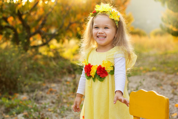 Little girl is sitting on chair in autumn garden