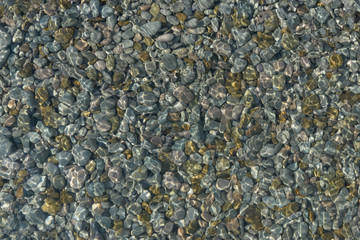 Shimmering sun glares on pebble seabed under water as background