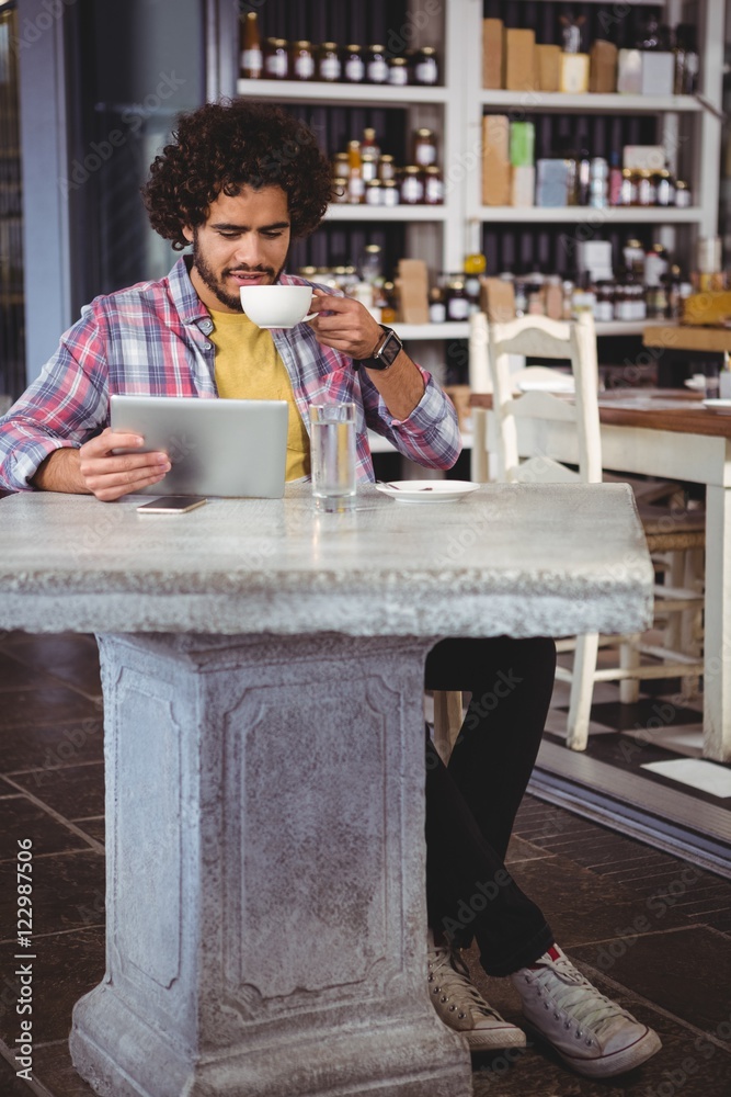 Poster man having coffee while looking at digital tablet