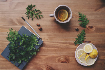 top view of notebook and pine branches with cup of tea with lemons