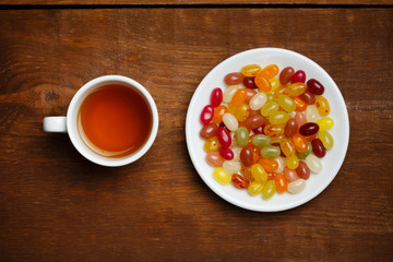 Cup of tea and plate with candies on wooden table