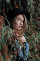 Fototapeta na wymiar lonely sad pretty cute blond girl with blue eyes and full lips in black hat and coat walking in autumn forest