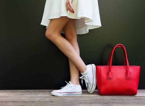 beautiful fashionable big red handbag standing next to leggy woman in white short dress and white sneakers