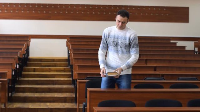 The student enters the lecture hall. He sits at the desk. He turns over the pages of the books.