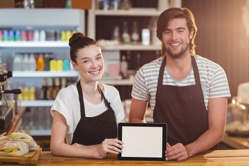 Smiling waiter and waitress using digital tablet at counter