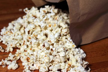 Fresh butter popcorn spills out of a brown paper bag and onto a wooden table - a classic movie snack.