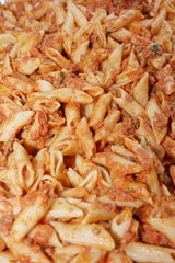 Tray of penne ala vodka macaroni pasta dish serving people at a party. background image.