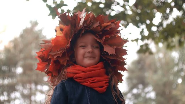 4k close-up portrait of happy smiling beautiful cute little girl in a wreath crown of autumn maple leaves